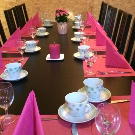 Festlich gedeckter Kaffeetisch mit rosa Servietten, Tassen, Gläsern und rosa Kerze in der Mitte.