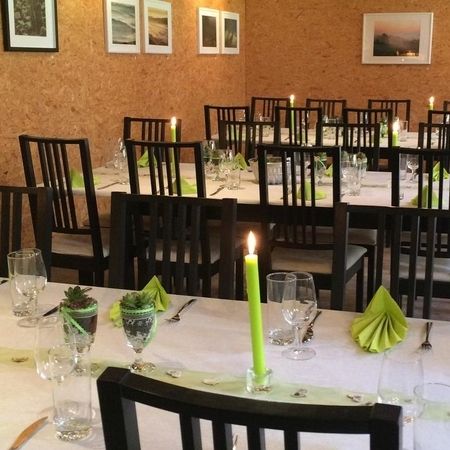 Mehrere gedeckte Tische mit grünen Servietten, Kerzen und Sukkulenten als Tischdekoration.